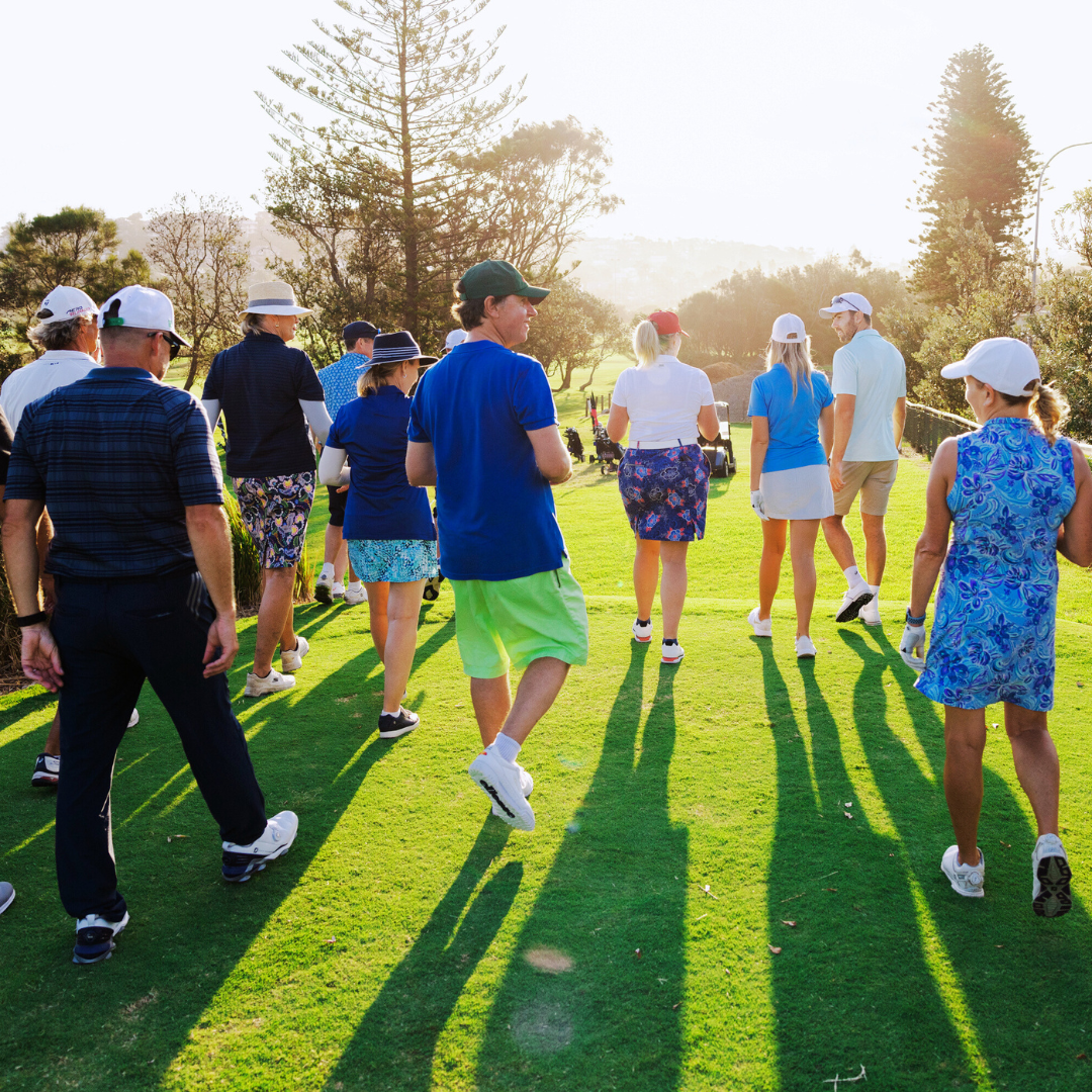 A group of golfers walk together across a sunlit fairway, casting long shadows on the grass.